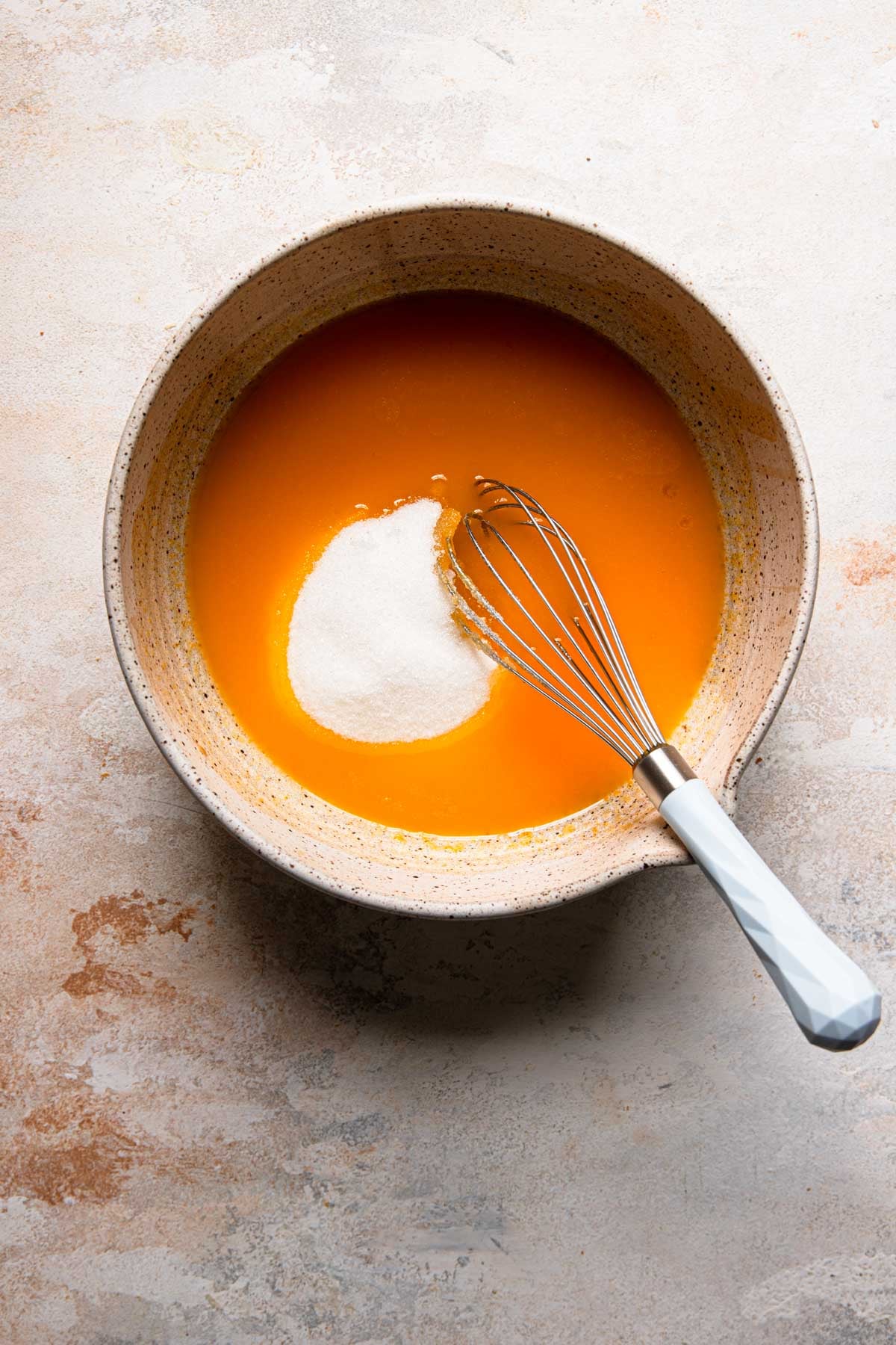 A large bowl with egg yolks mixture, sugar and a whisk.