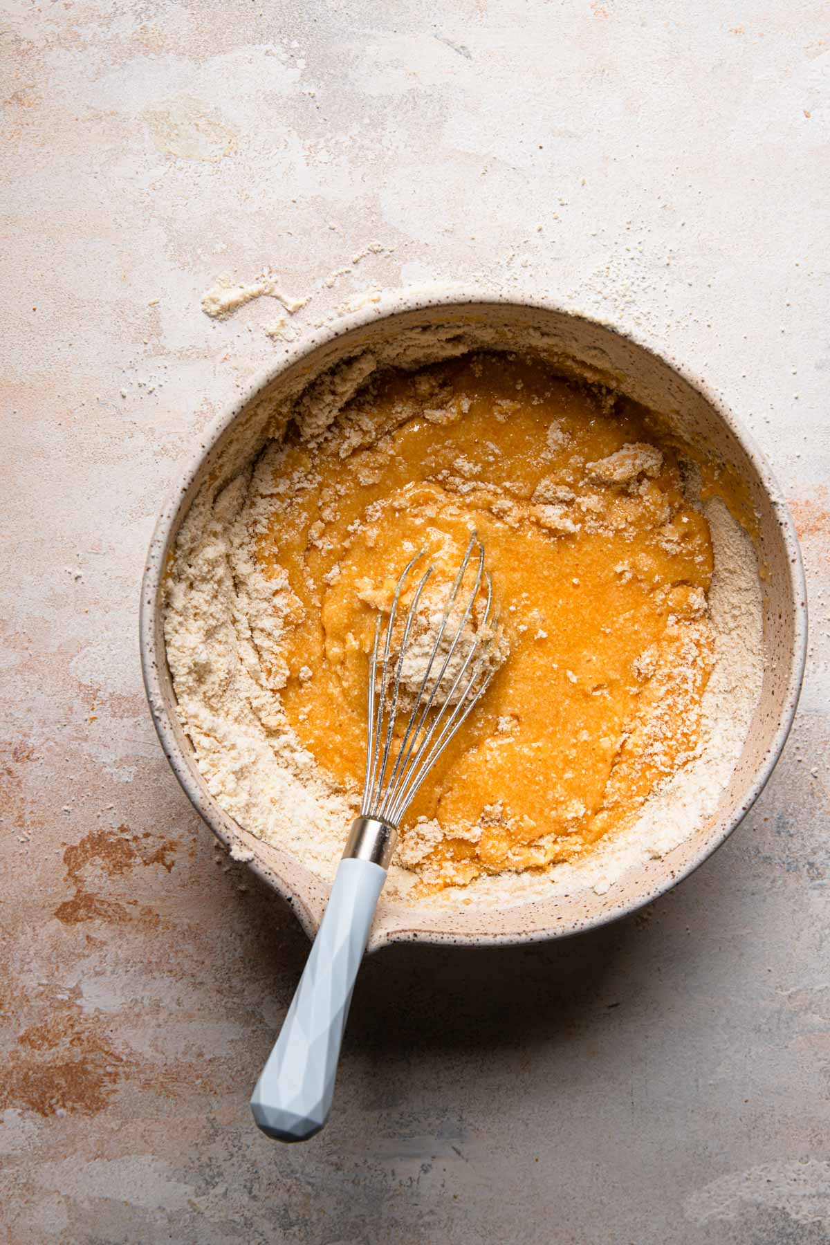 A large bowl with egg yolk mixture and a whisk mixing in almond flour.