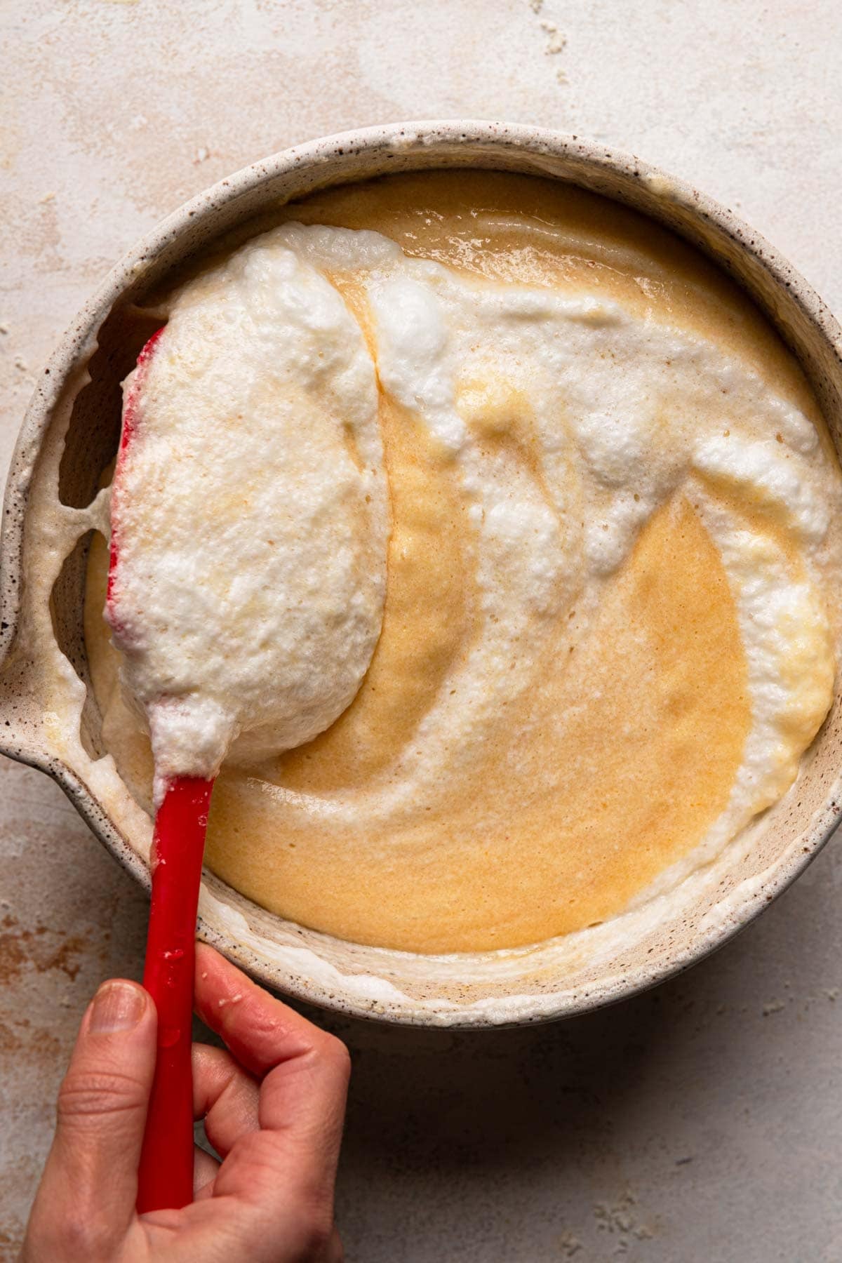A hand folding  meringue into cake batter.