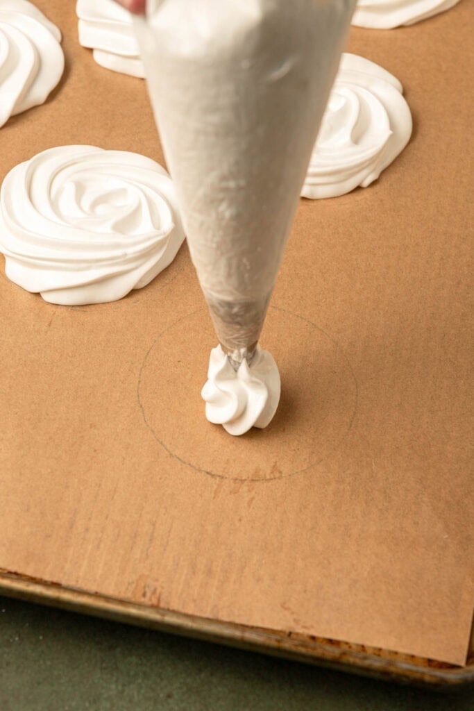 Piping meringue over a plan lined with parchment paper.