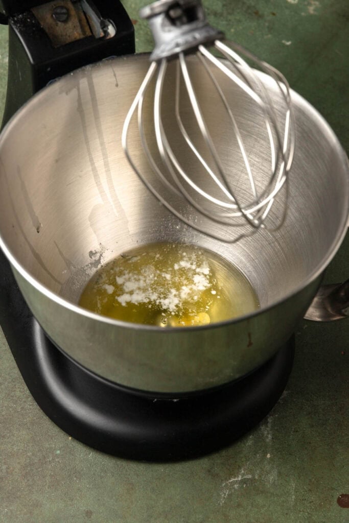 A stand mixer bowl with egg whites and a cream of tartar with the whisk attachment.
