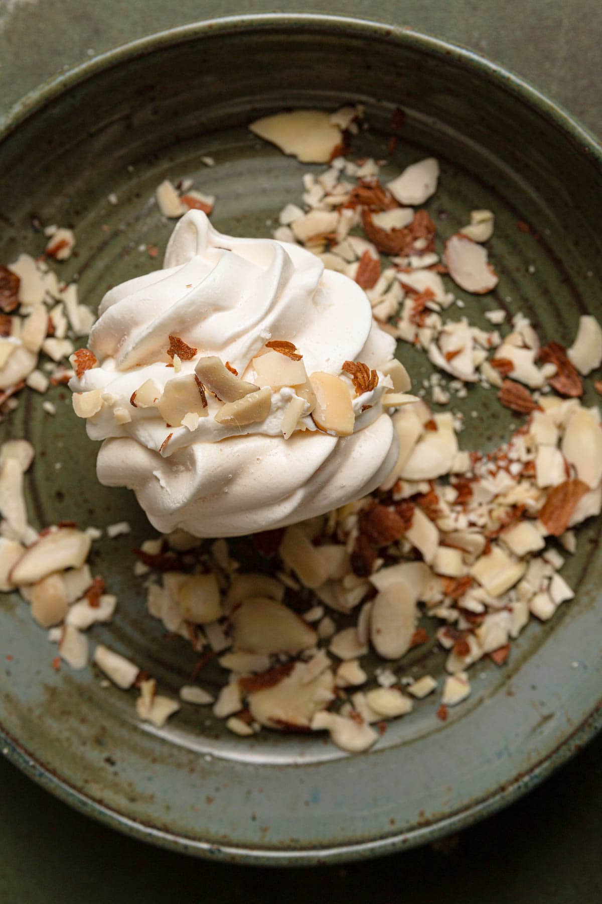 Two meringue cookies filled with cream in a bowl with sliced almonds.