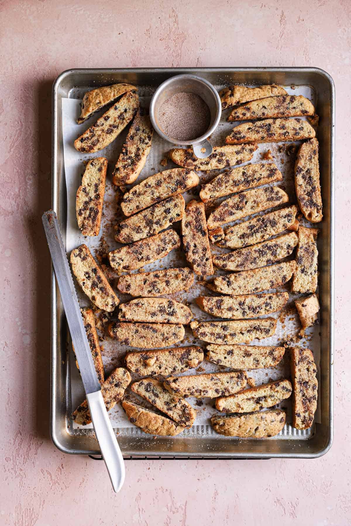A baking sheet with mandel bread cookies and a serrated knife.