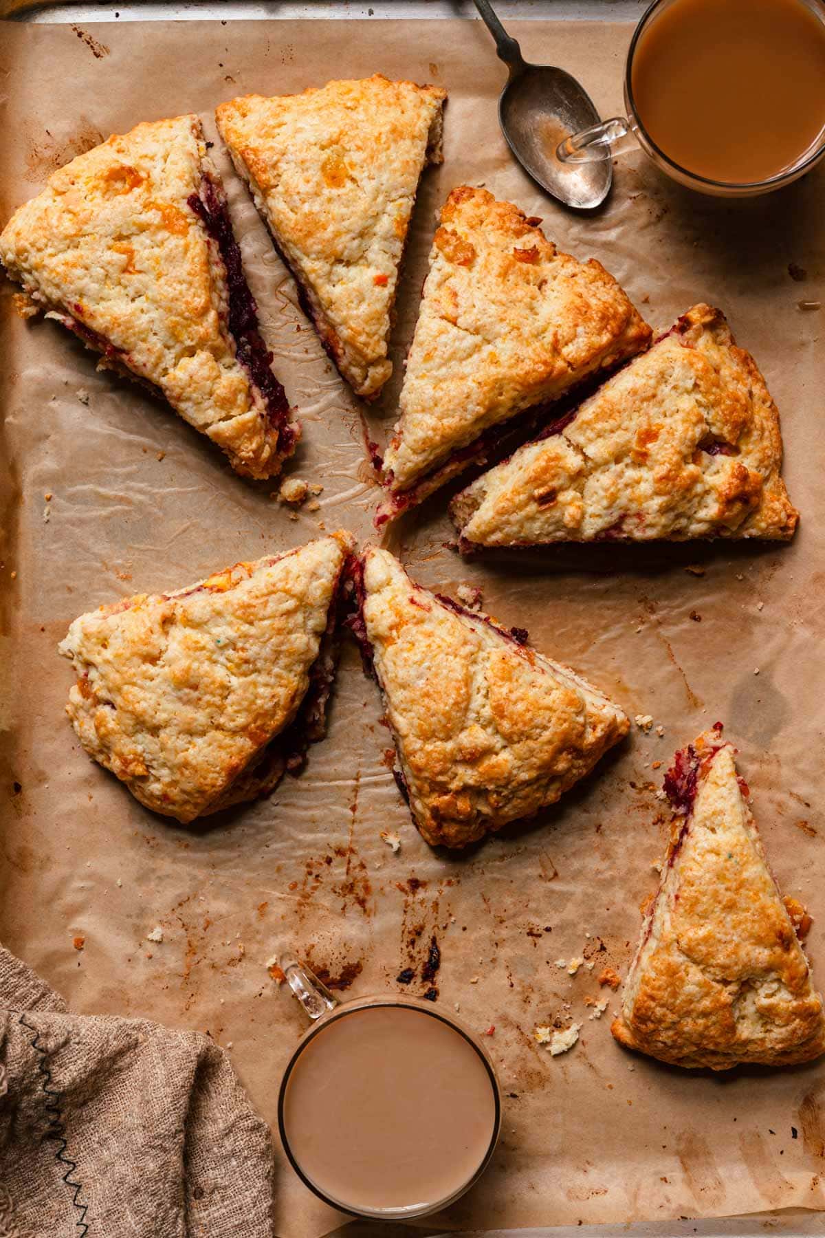 orange cranberry scones over a pan with parchment paper and coffee cups.