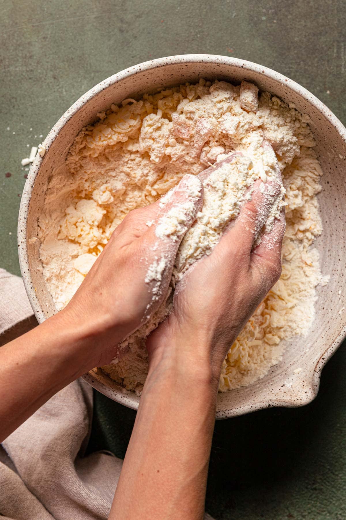Hands rubbing butter into flour over a large mixing bowl.