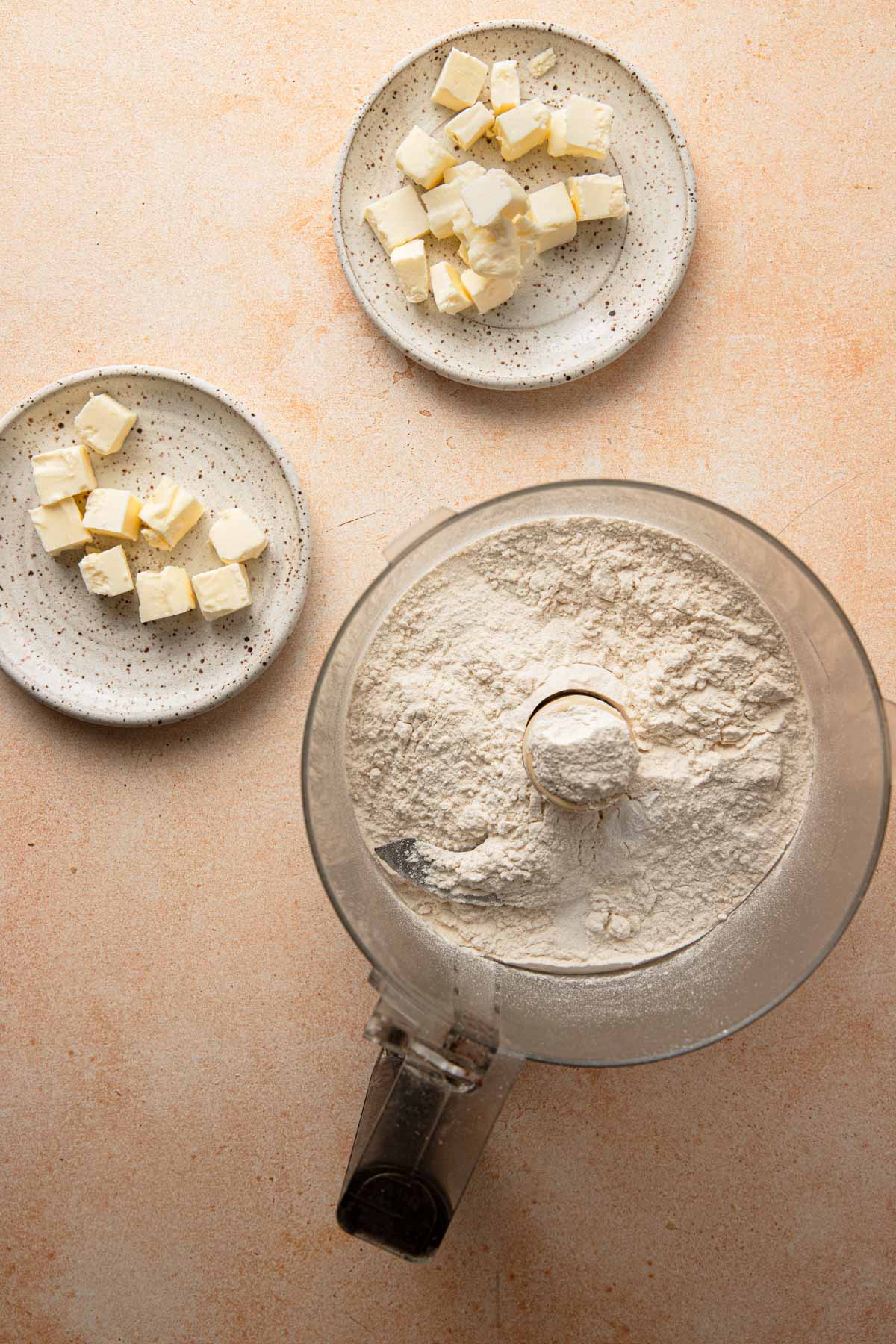 A food processor bowl with two plates with butter pieces.