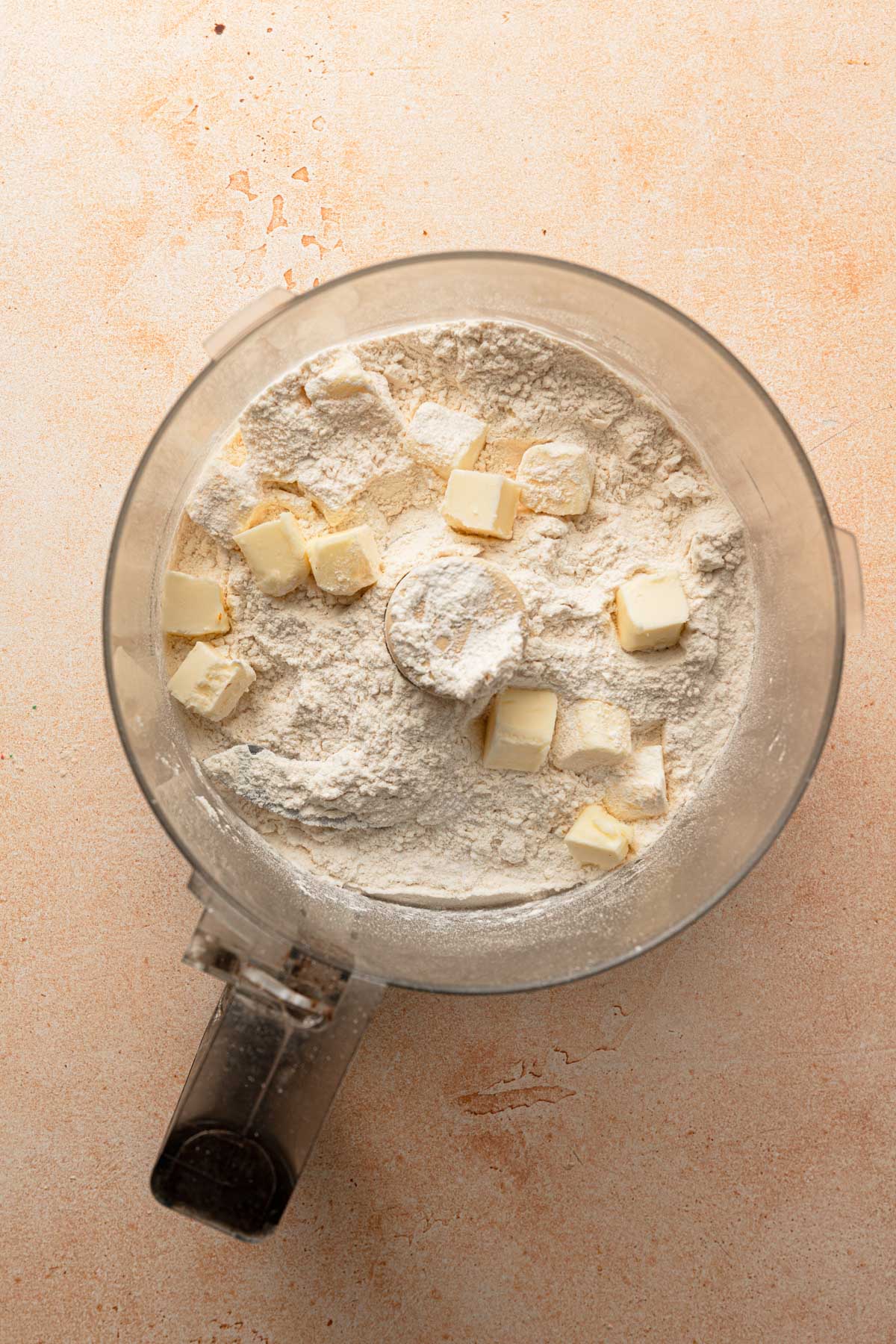 A food processor bowl with flour and butter chunks.