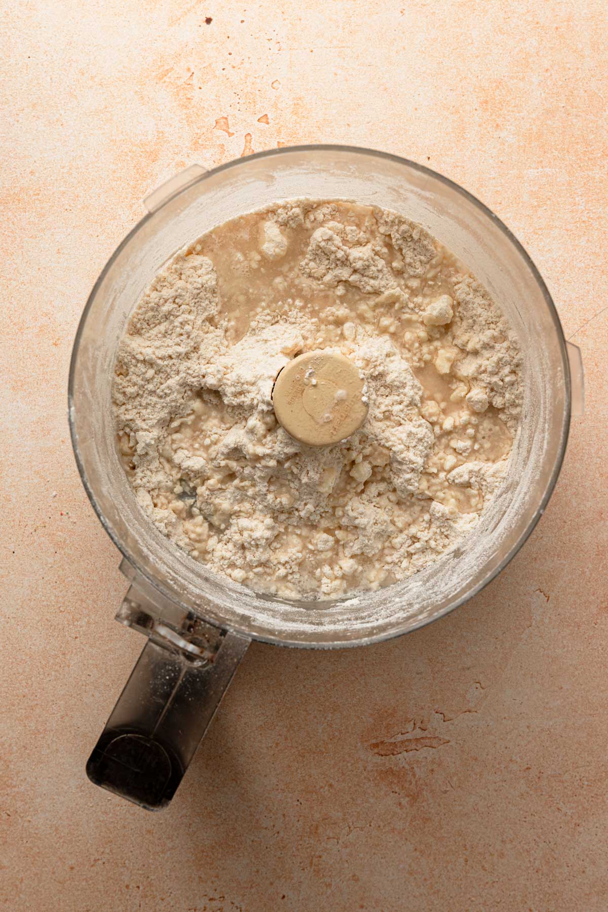 A food processor bowl with flour mixture and water on top.
