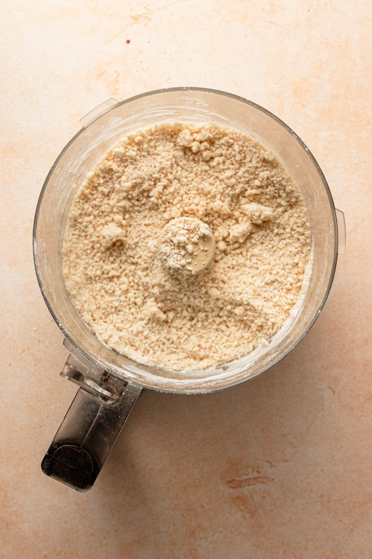 A food processor bowl with flour mixture for pie.