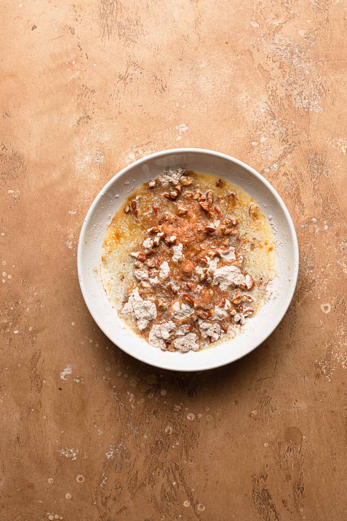 A bowl with flour, melted butter and chopped pecans.