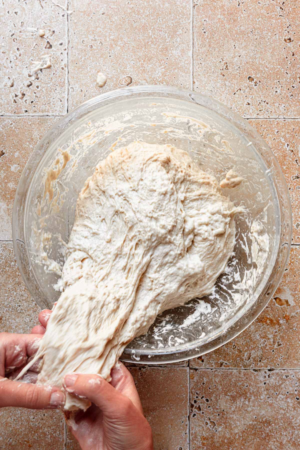 Hands stretching dough in a bowl.