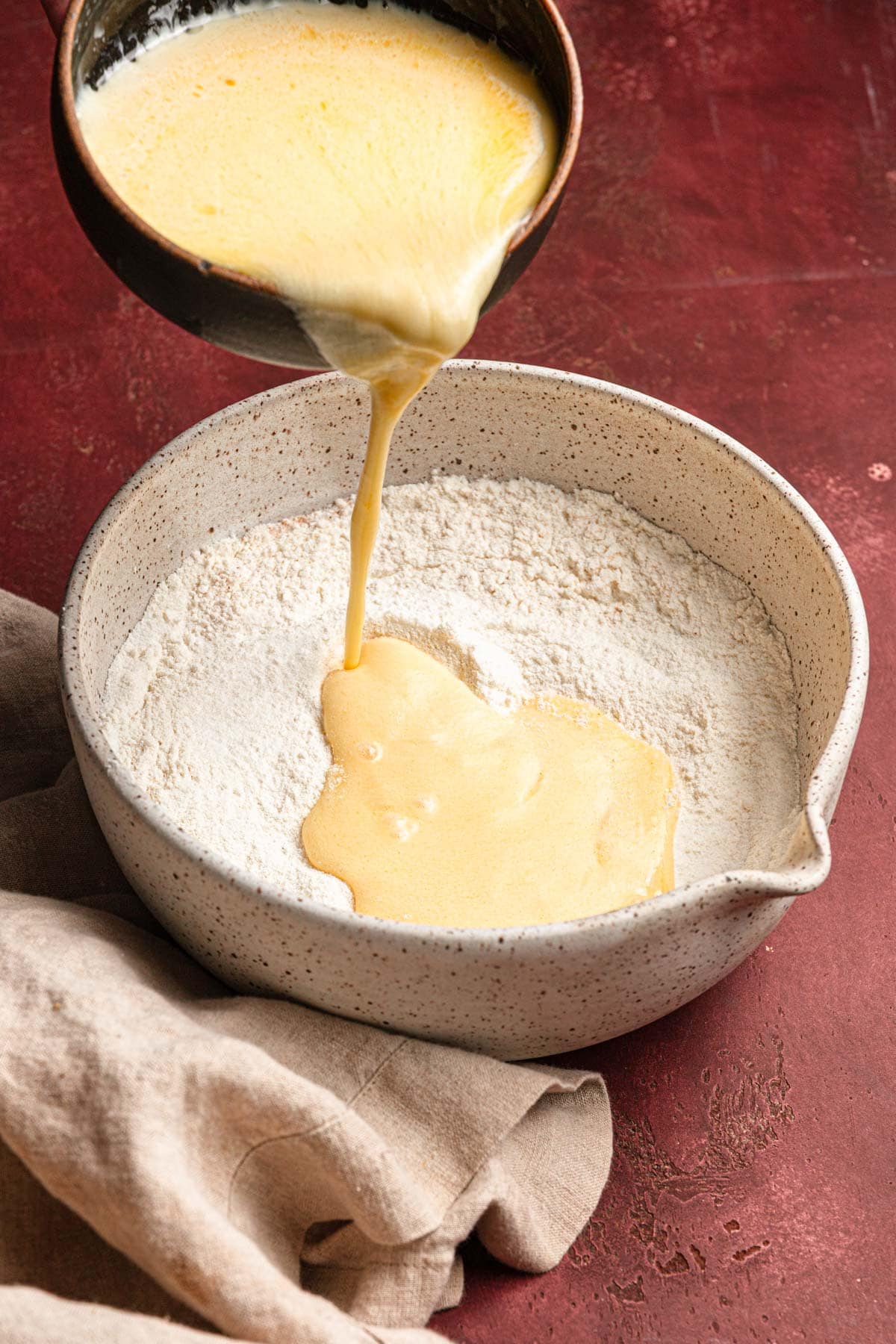 Pouring eggnog mixture into a bowl with flour.