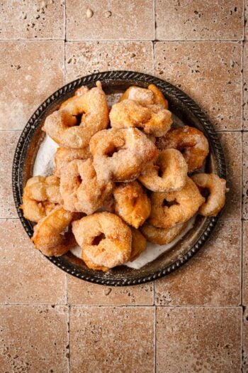 Sfenj donuts coated with oil on a plate.