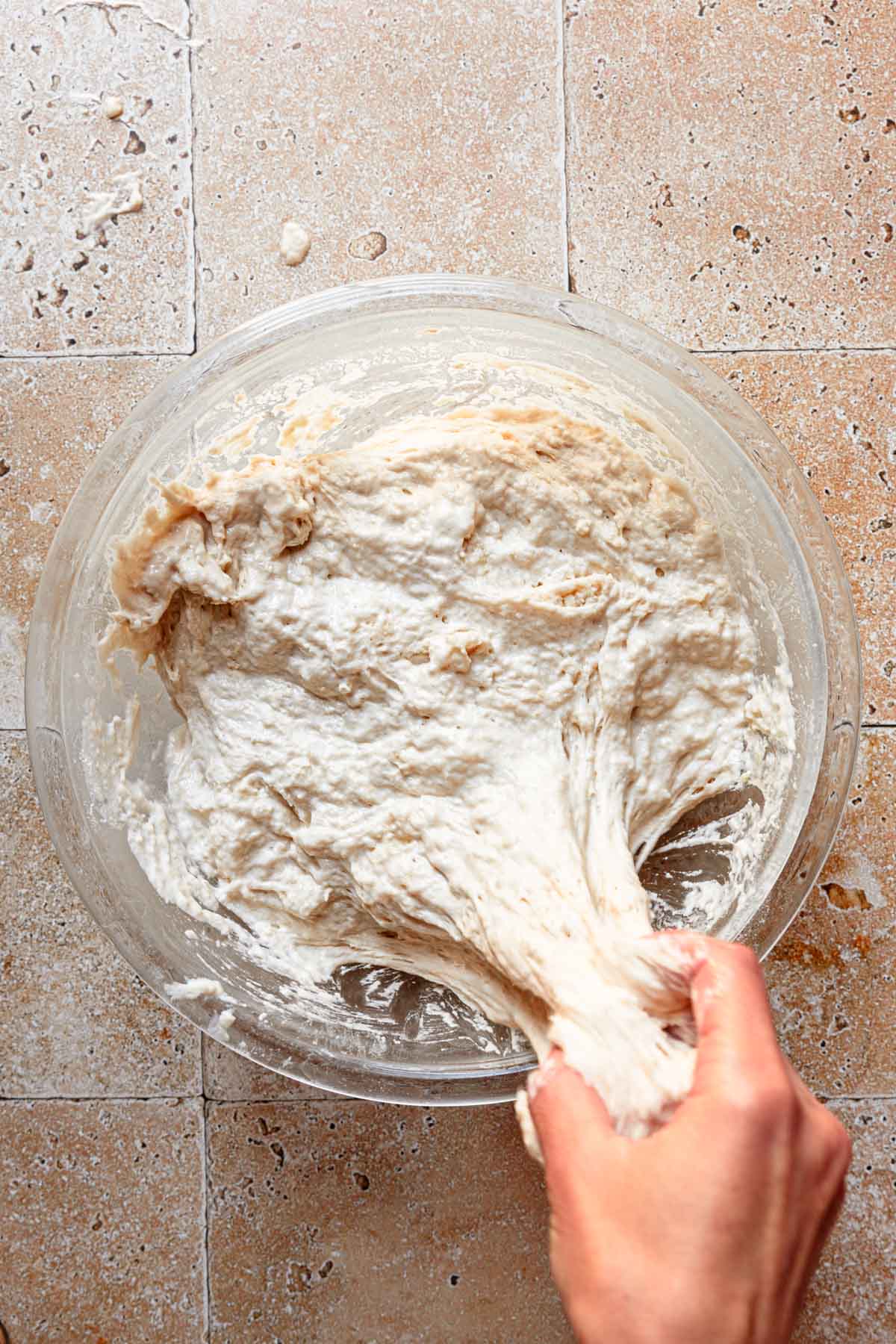 Hands stretching dough in a bowl.