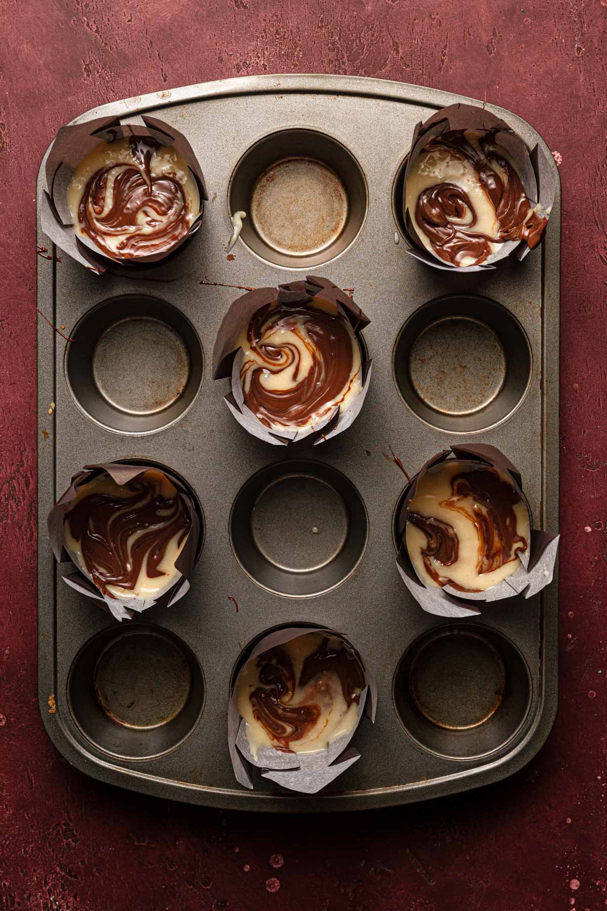 A pan with unbaked muffins swirled with chocolate.