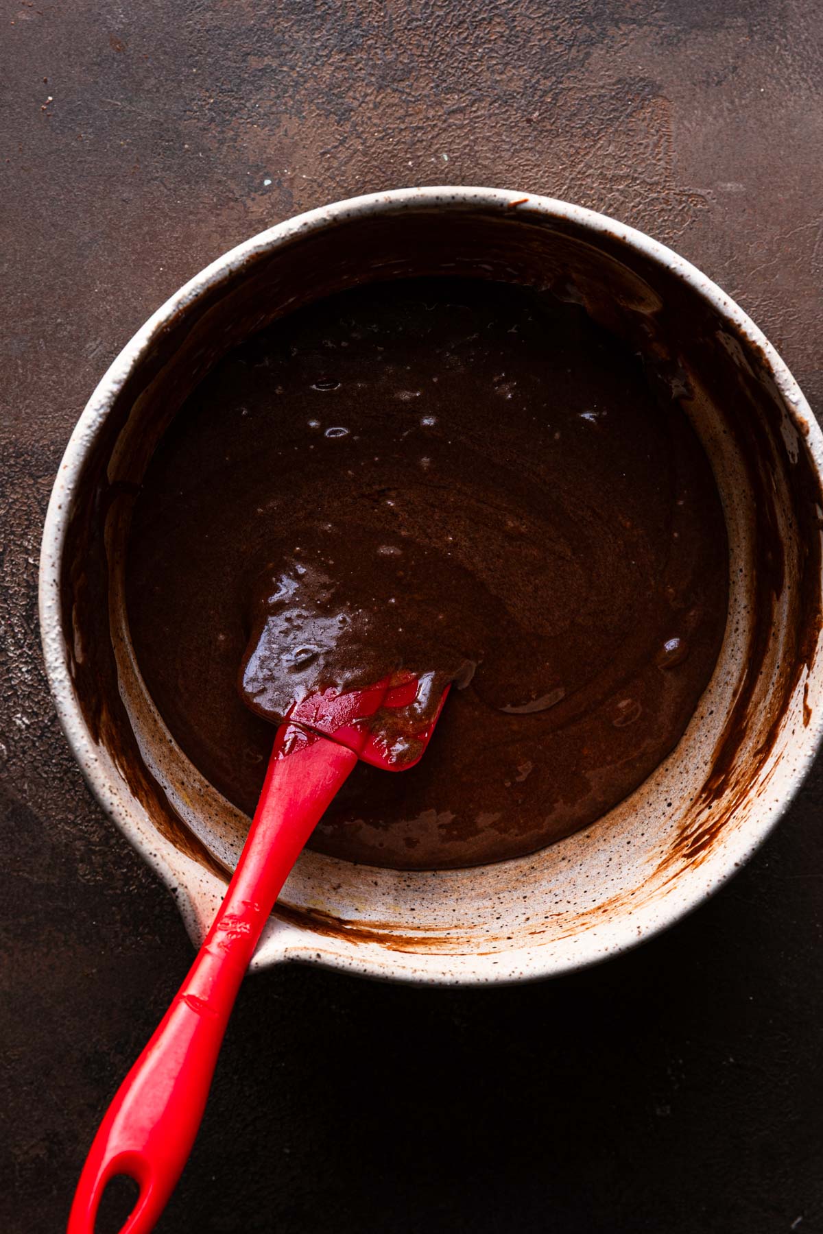 A bowl with chocolate batter and a spatula.