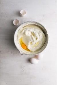A bowl with cheesecake mixture and an egg