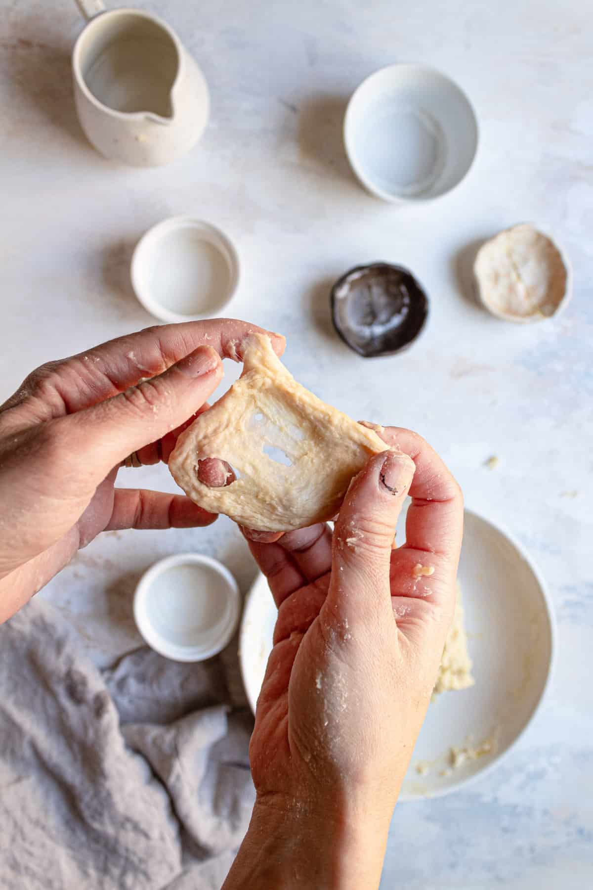 Hands holding a piece of stretched dough with holes in the middle.