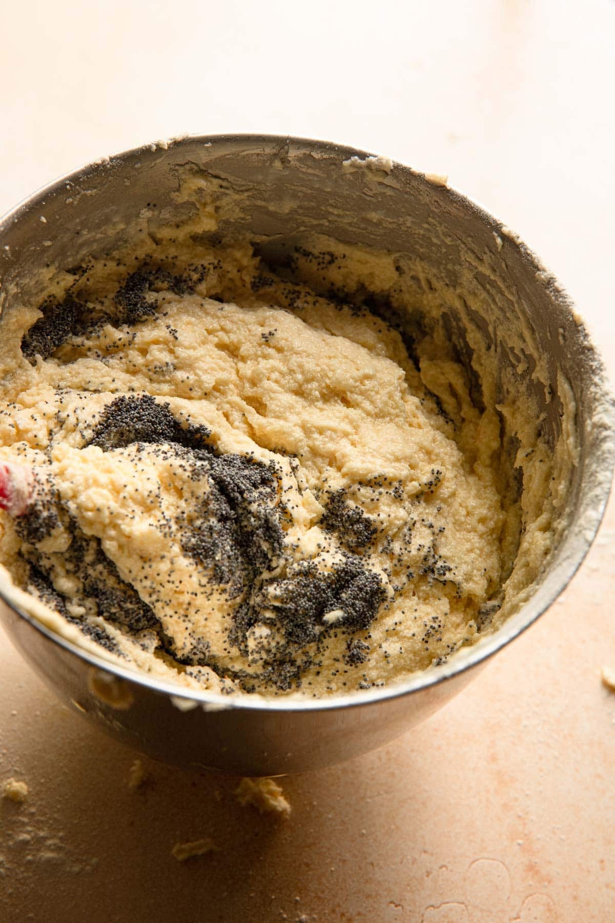 A stand mixer bowl with cake batter and poppy seeds.