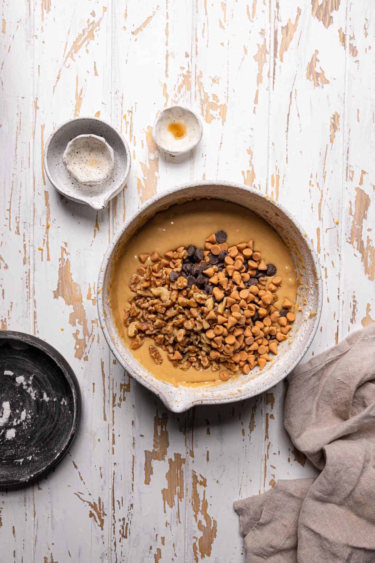 A large bowl with blondie batter, chocolate chips, butterscotch chips and chopped nuts.