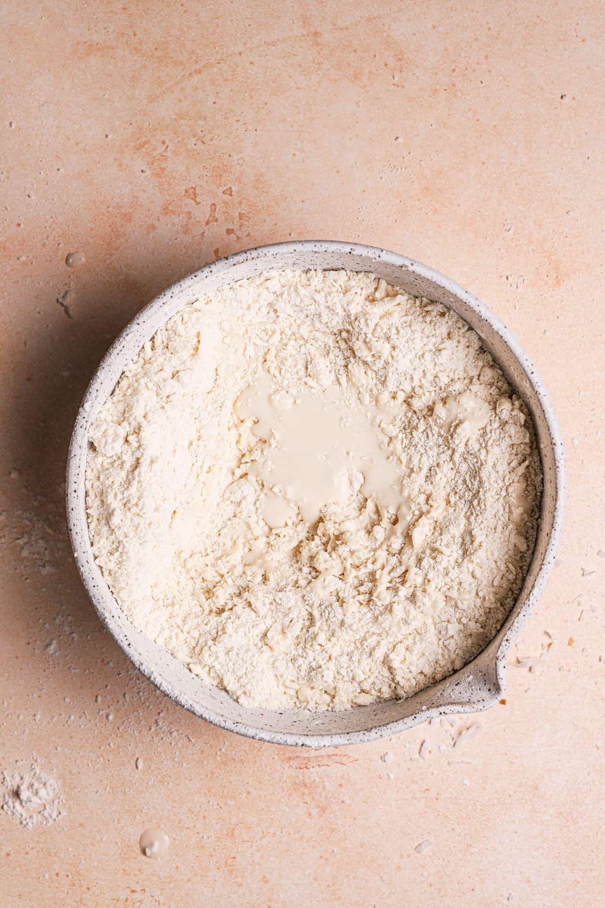 A mixing bowl with flour coated with butter and coconut milk over it.