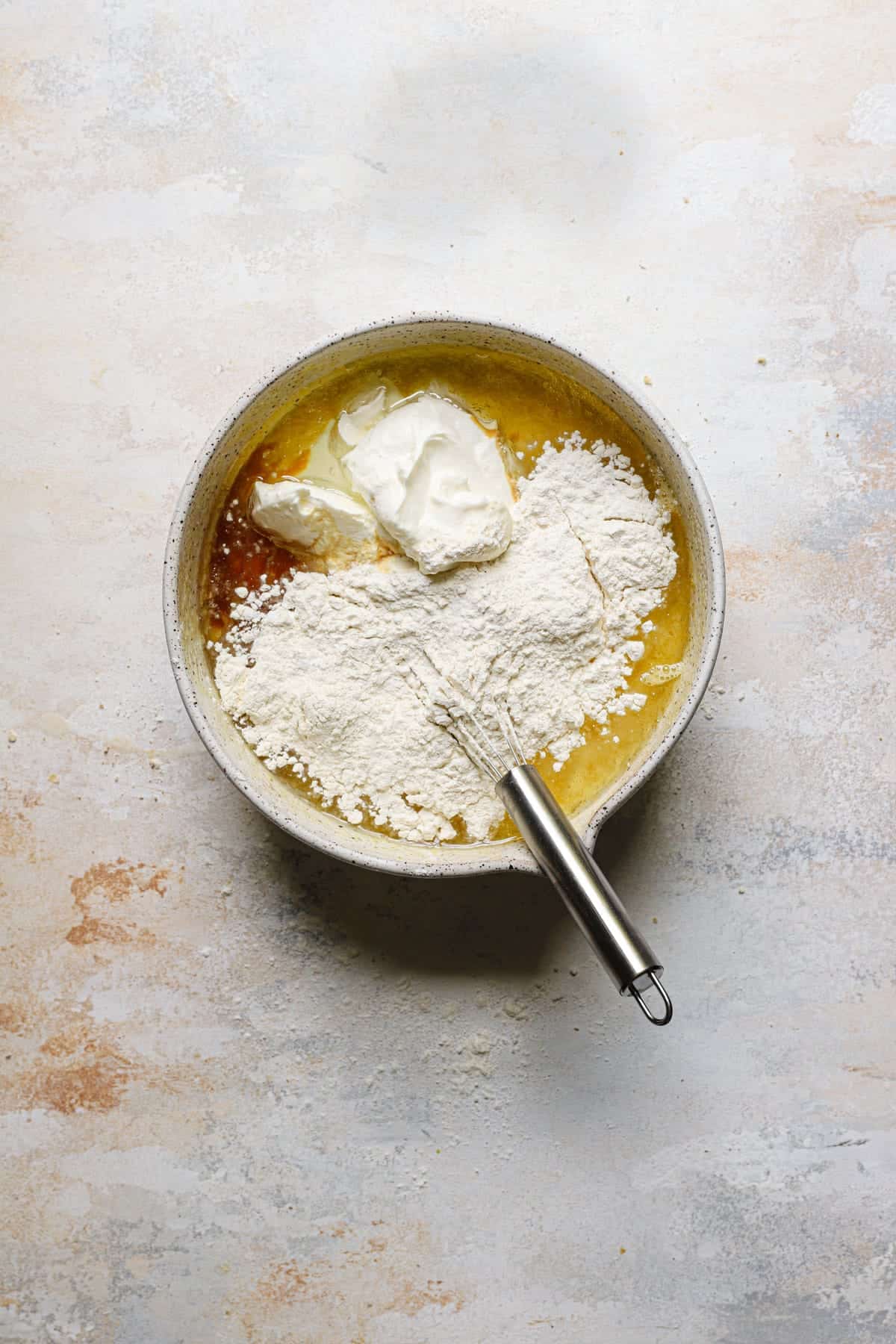 A mixing bowl with eggs, sugar, flour and a whisk.