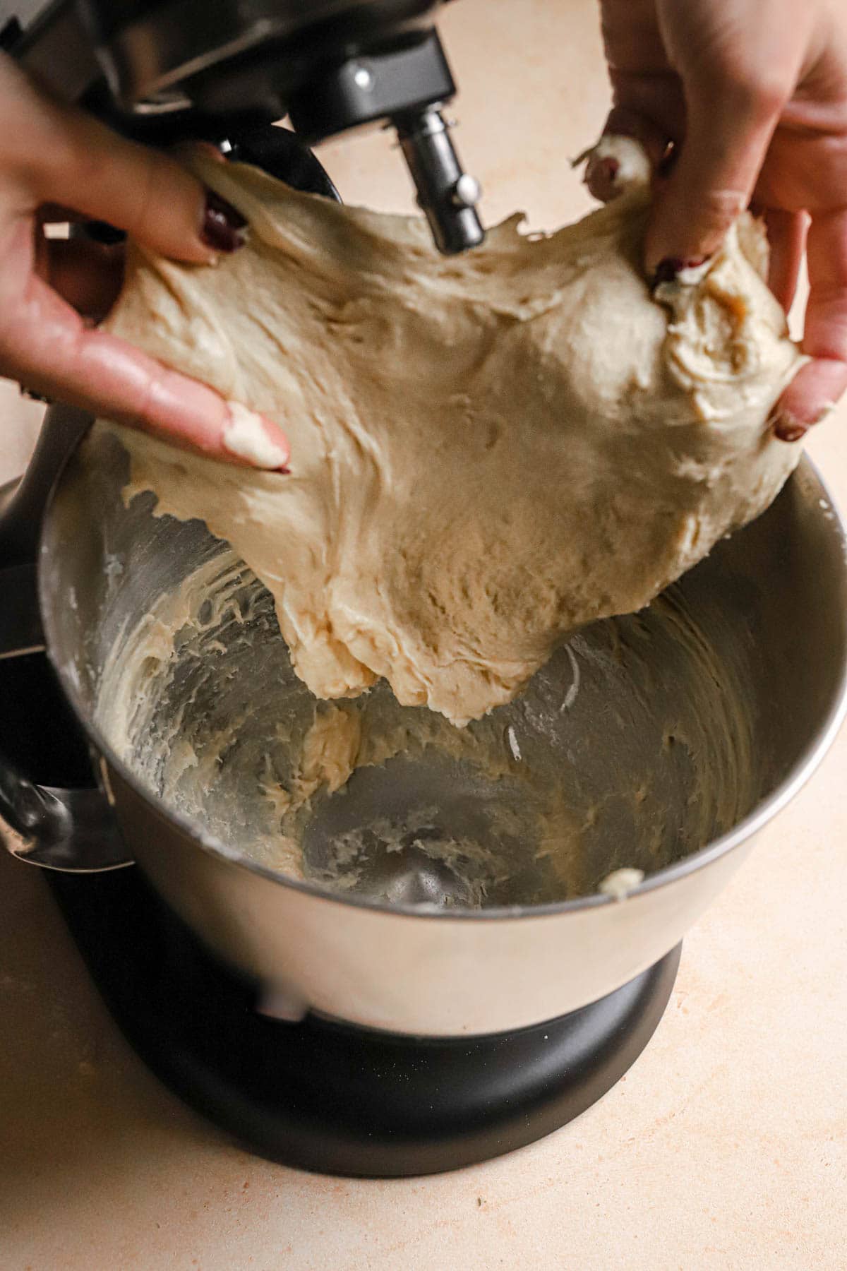 Hands stretching brioche dough from a stand mixer bowl.