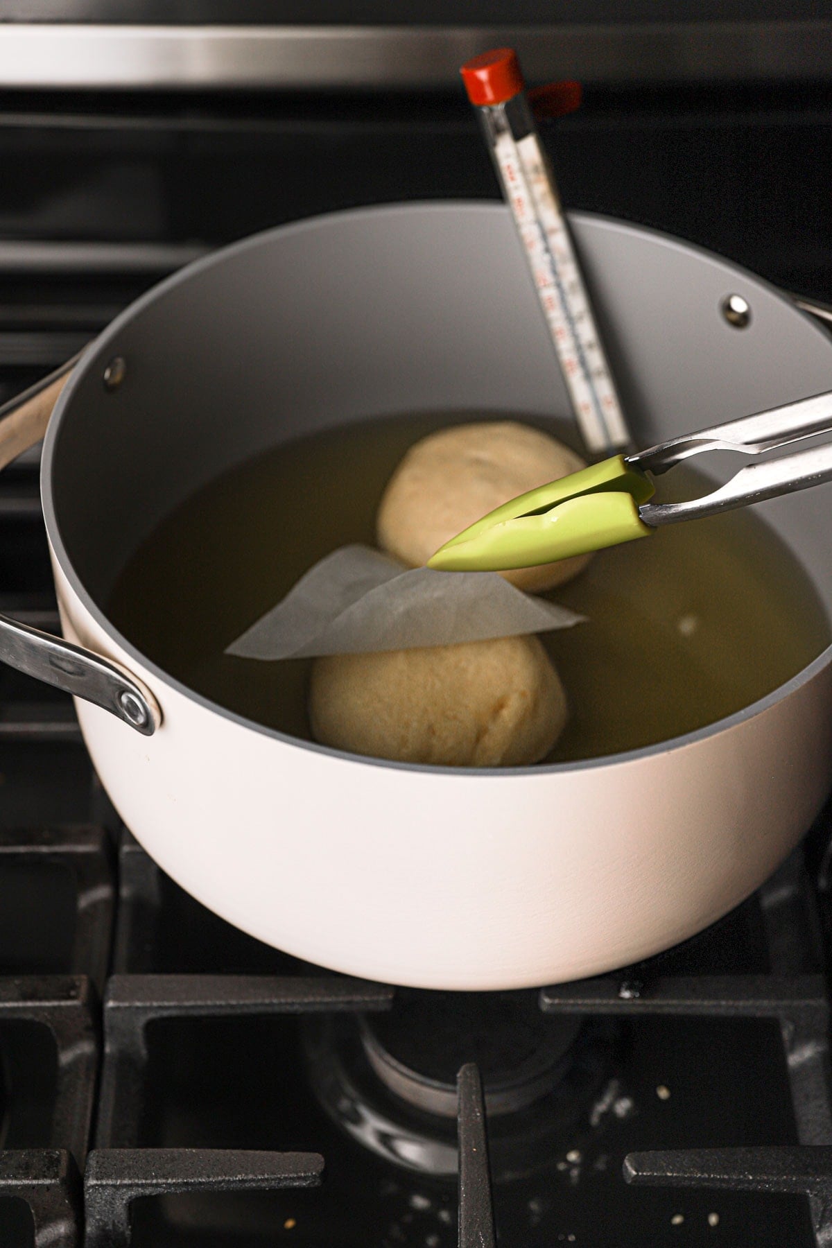 Kitchen tongs removing parchment paper from a donut in a pan with oil.
