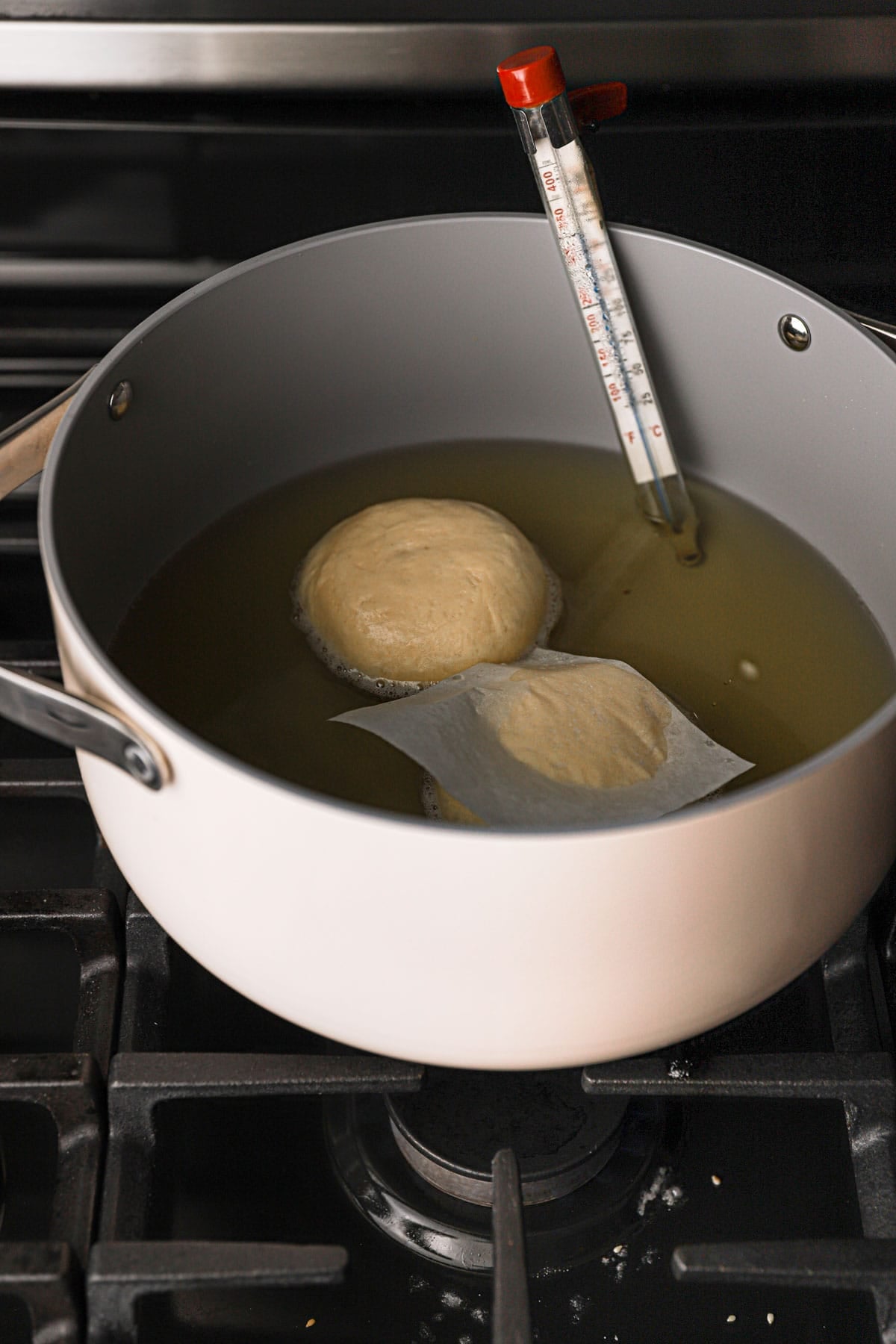 A wide pan filled with oil, and a thermometer with two donuts.