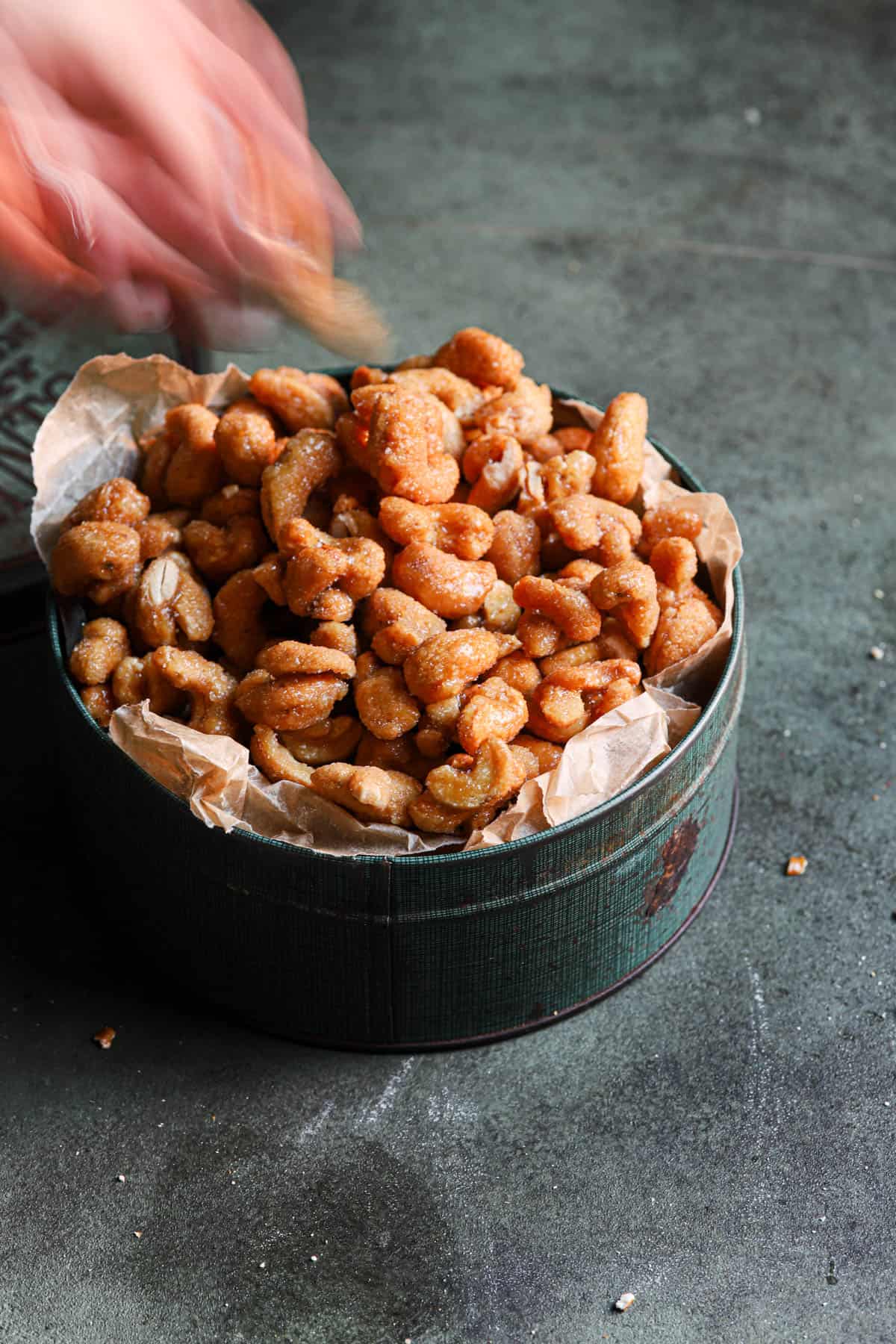 a hand reaching to a box full of sweet nuts