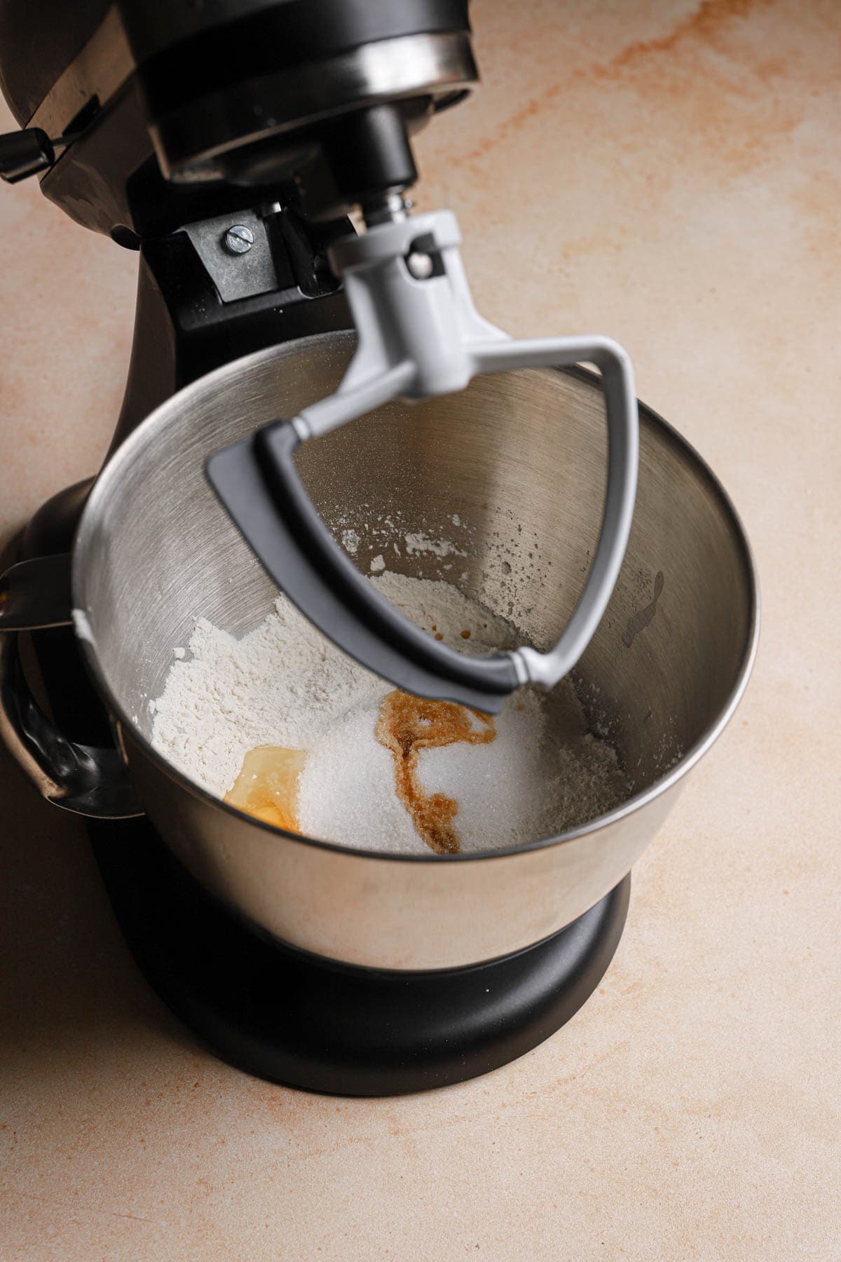 A stand mixer with the paddle attachment and flour in the bowl.