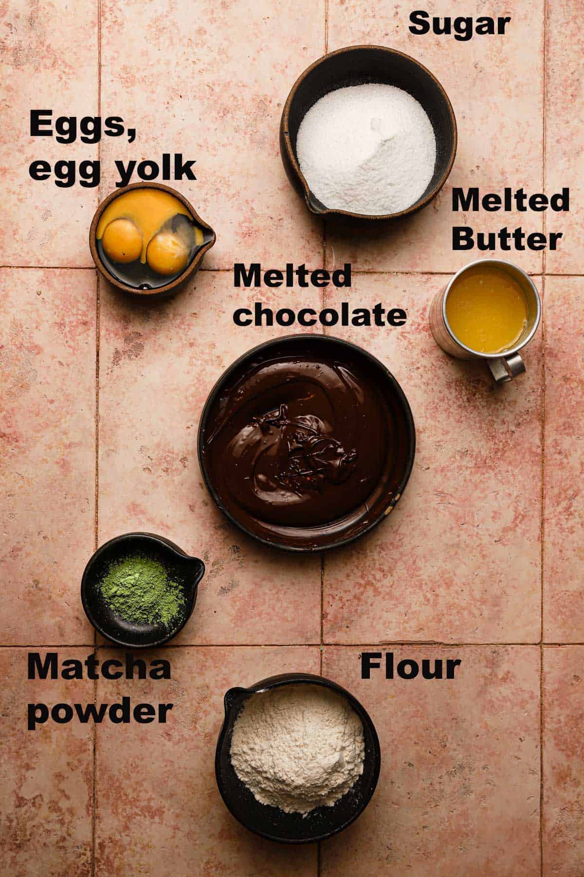 Ingredients in bowls melted chocolate, matcha powder, flour, melted butter, eggs, sugar