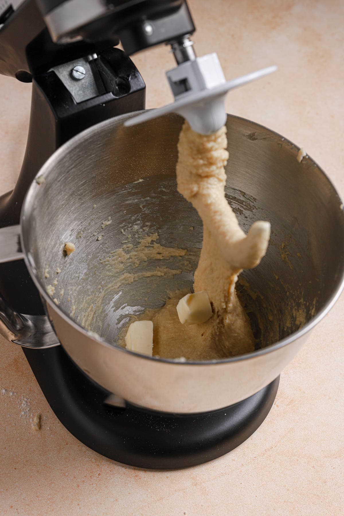 A stand mixer with dough and pieces of butter. 