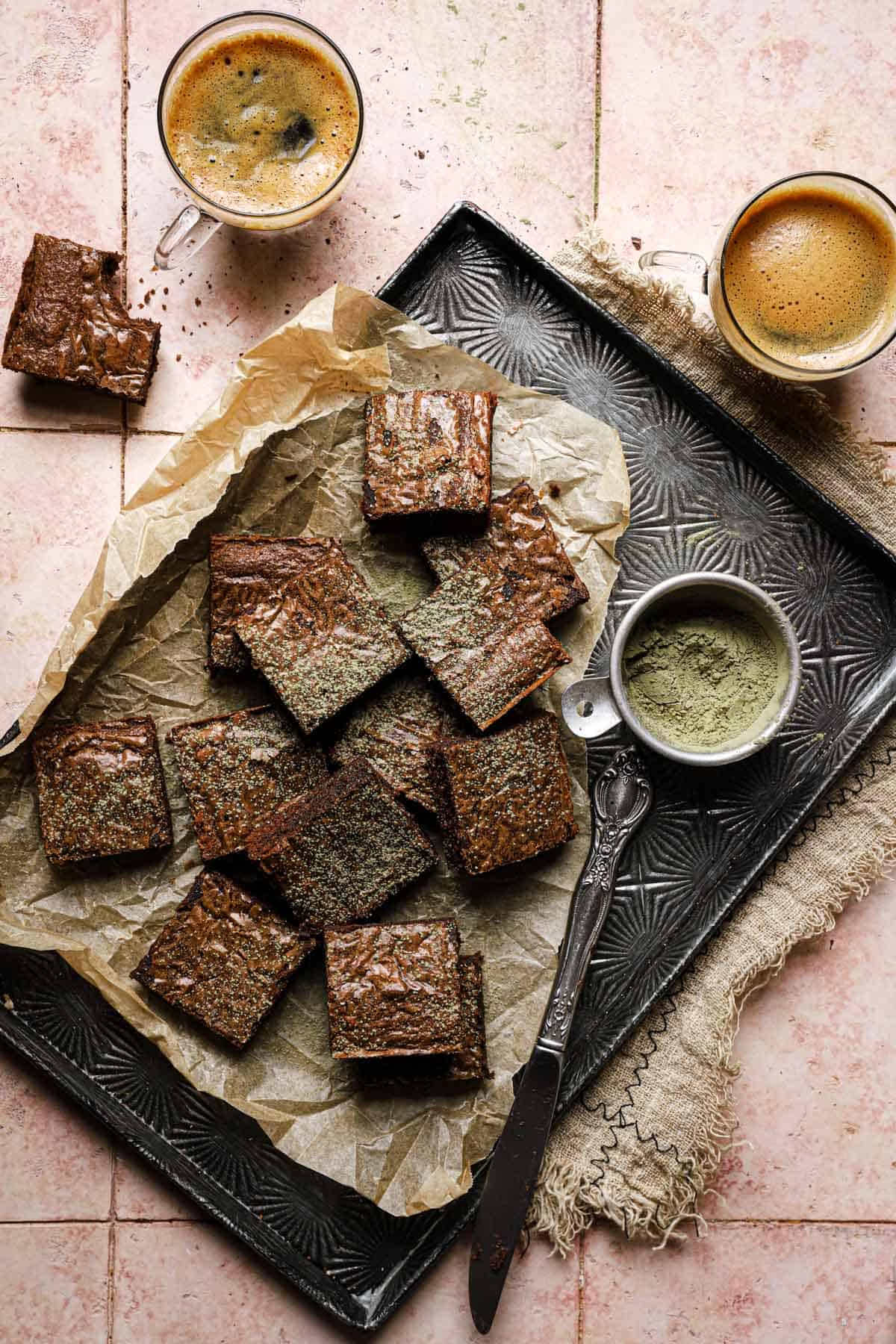 chocolate bars in a pan dusted with matcha powder and coffee cups next to the pan