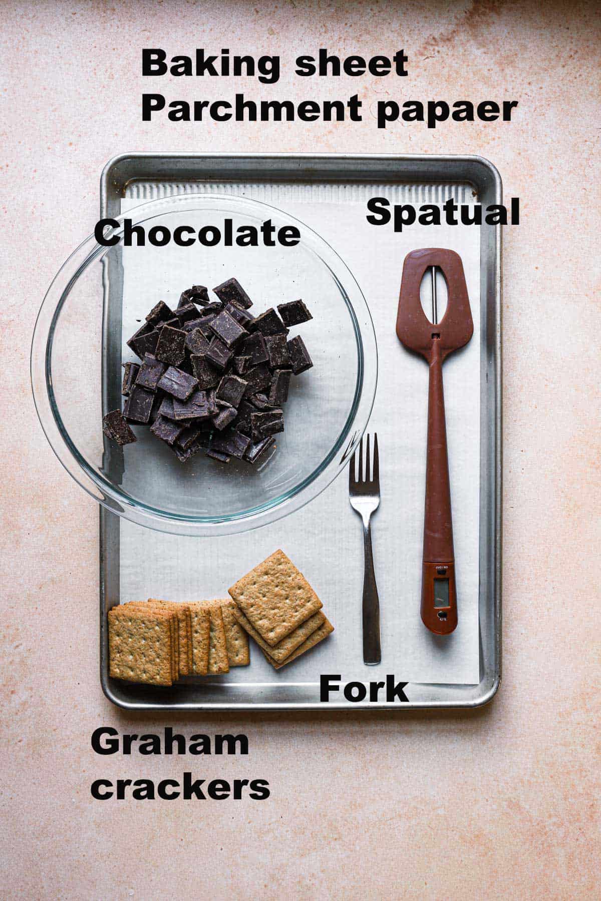 ingridiets and tools to make graham crackers covered with chocolate: a baking pan lined with parchment paper, a microwave safe bowl, chocolate, graham crackers, a spatula and a fork.