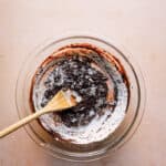 A wooden spoon in a bowl mixing in flour into brownie mixture