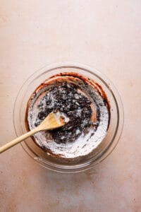 A wooden spoon in a bowl mixing in flour into brownie mixture