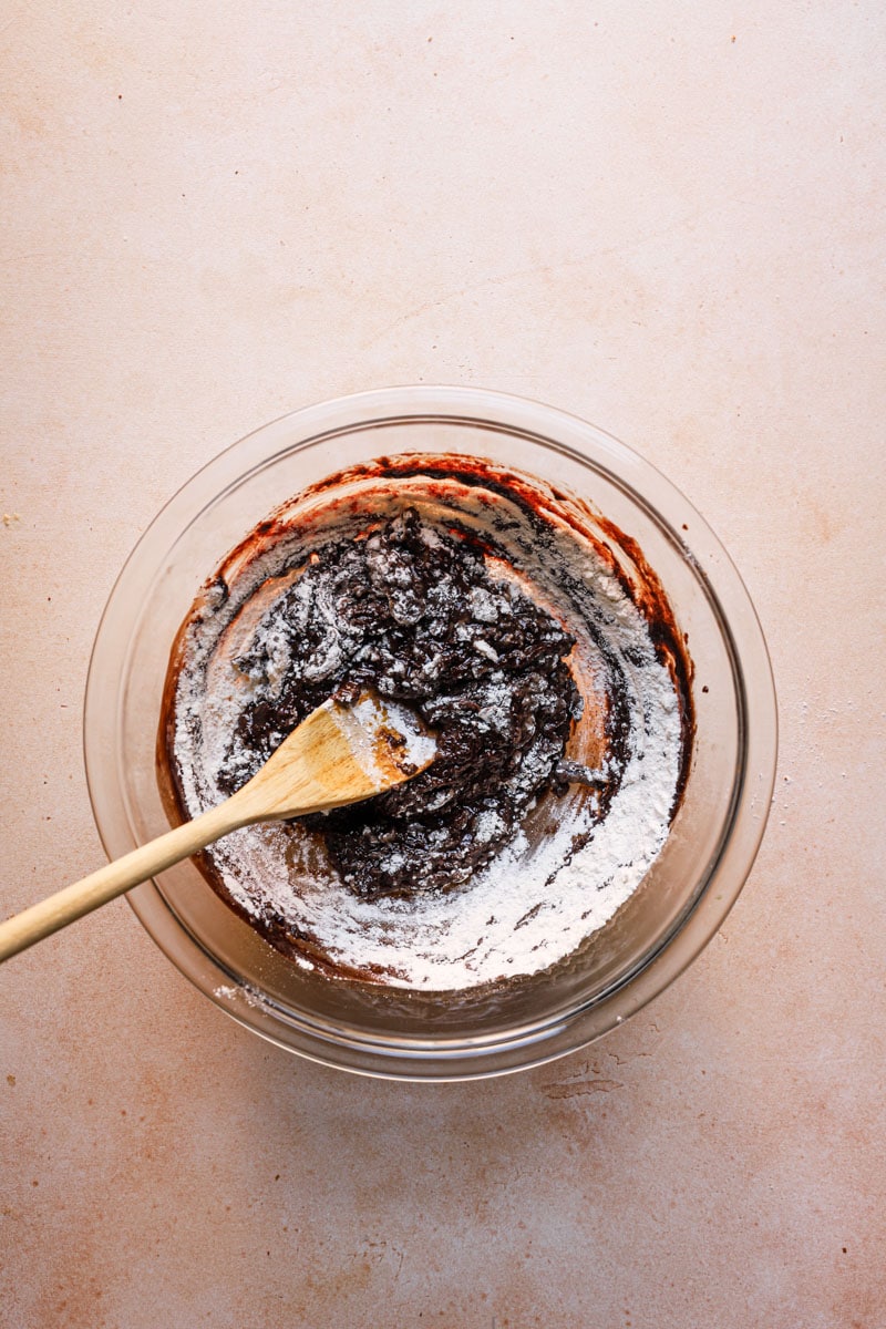 A bowl with brownie batter and a wooden spoon.