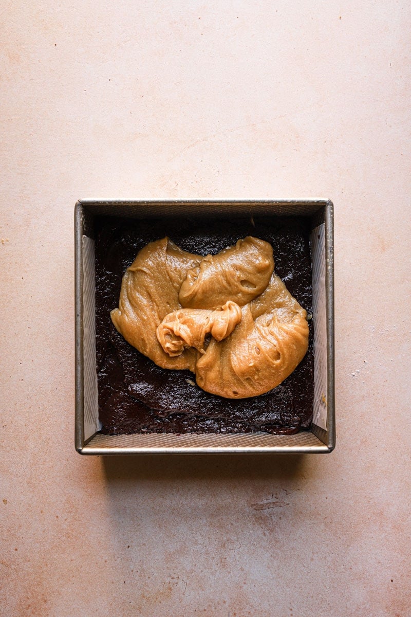An 8x8 square pan layered with brownie batter and blondie batter on top.