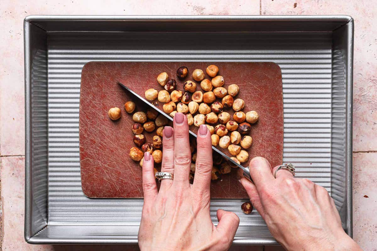 hand chopping hazelnuts placed inside a 9x13-inch pan.