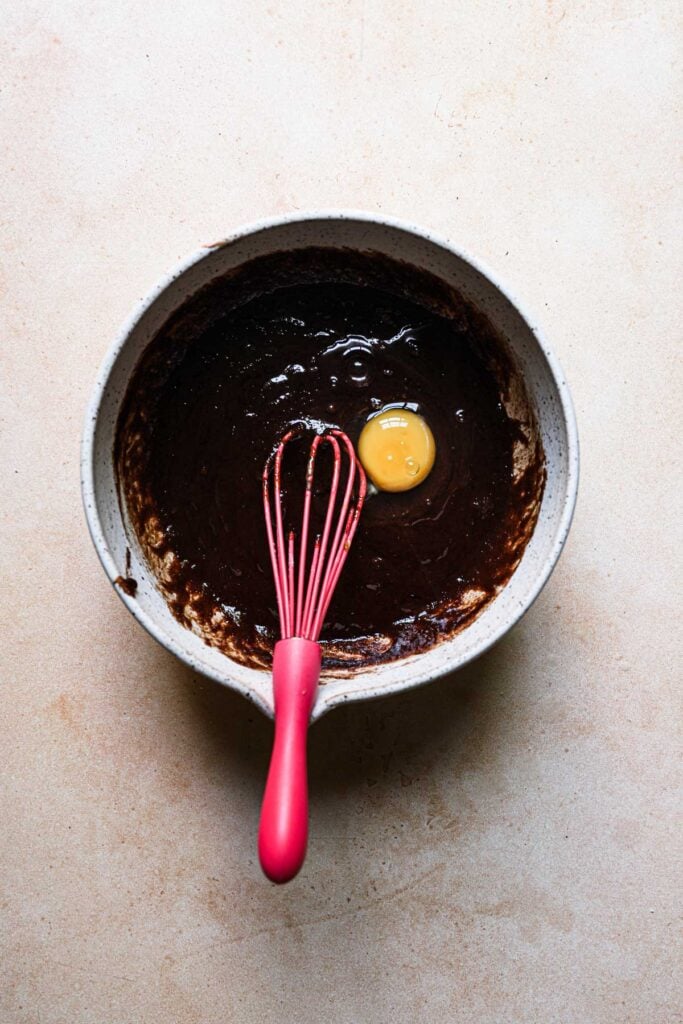 A bowl of melted chocolate with a whisk and an egg.