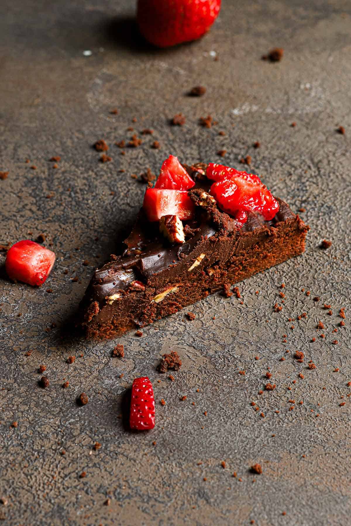 A slice of brownie topped with ganache and fresh strawberries.