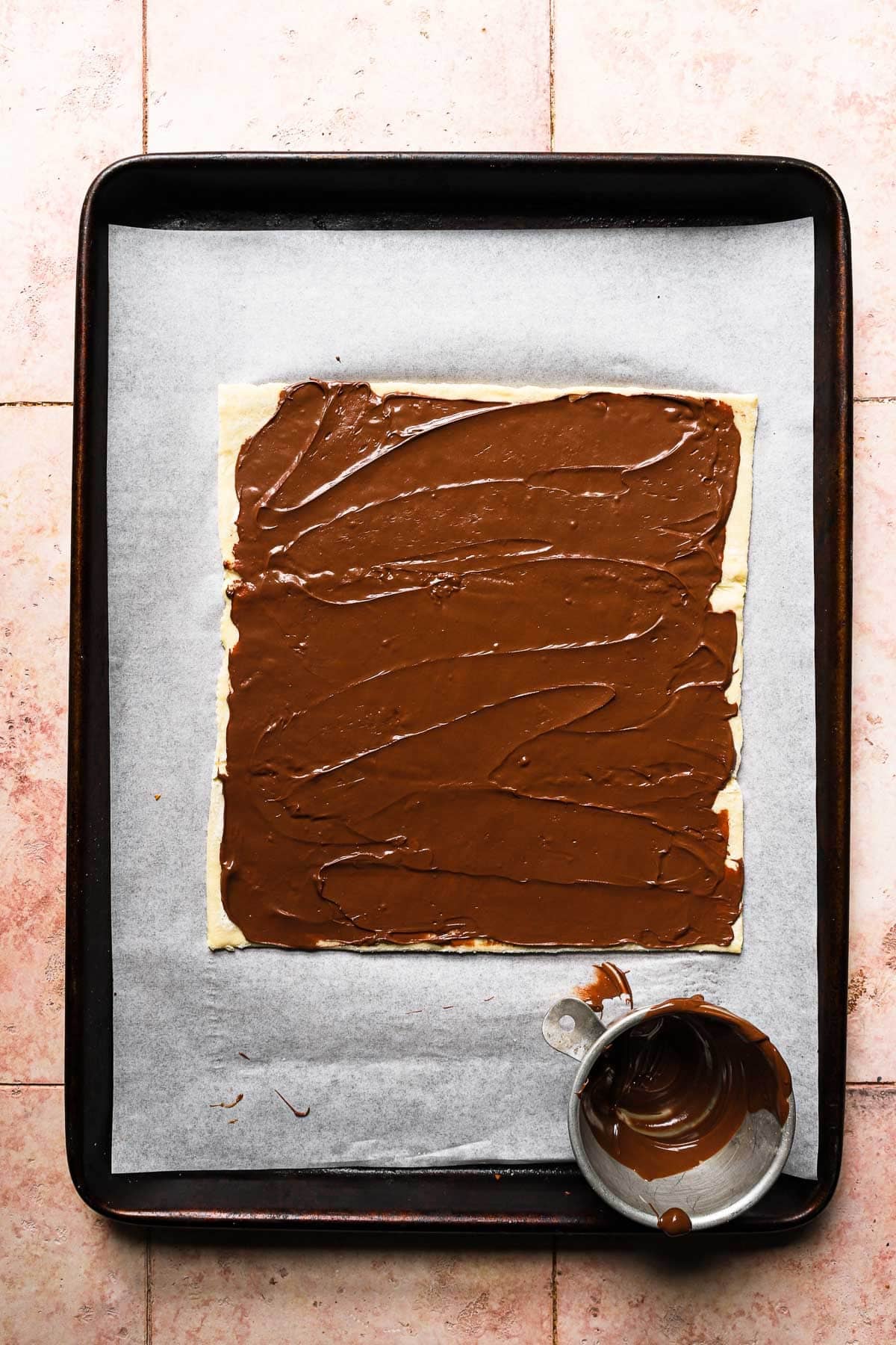 A baking sheet lined with parchment paper and topped with puff pastry spread with nutella.