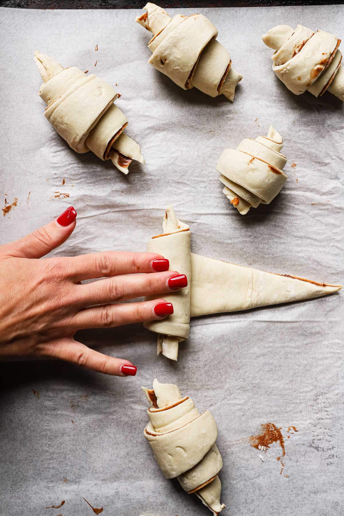 A hanf rolling a triangle dough into a croissant shape.