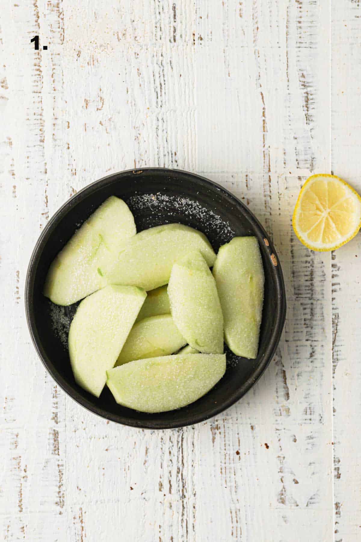 Sliced apples with sugar and lemon in a bowl.