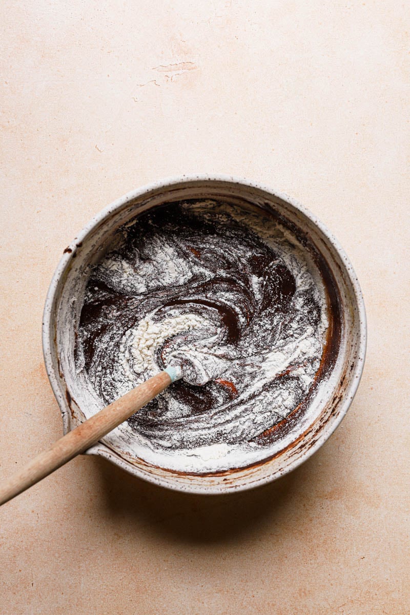 A bowl with brownies mixture and a spatula folding in flour.