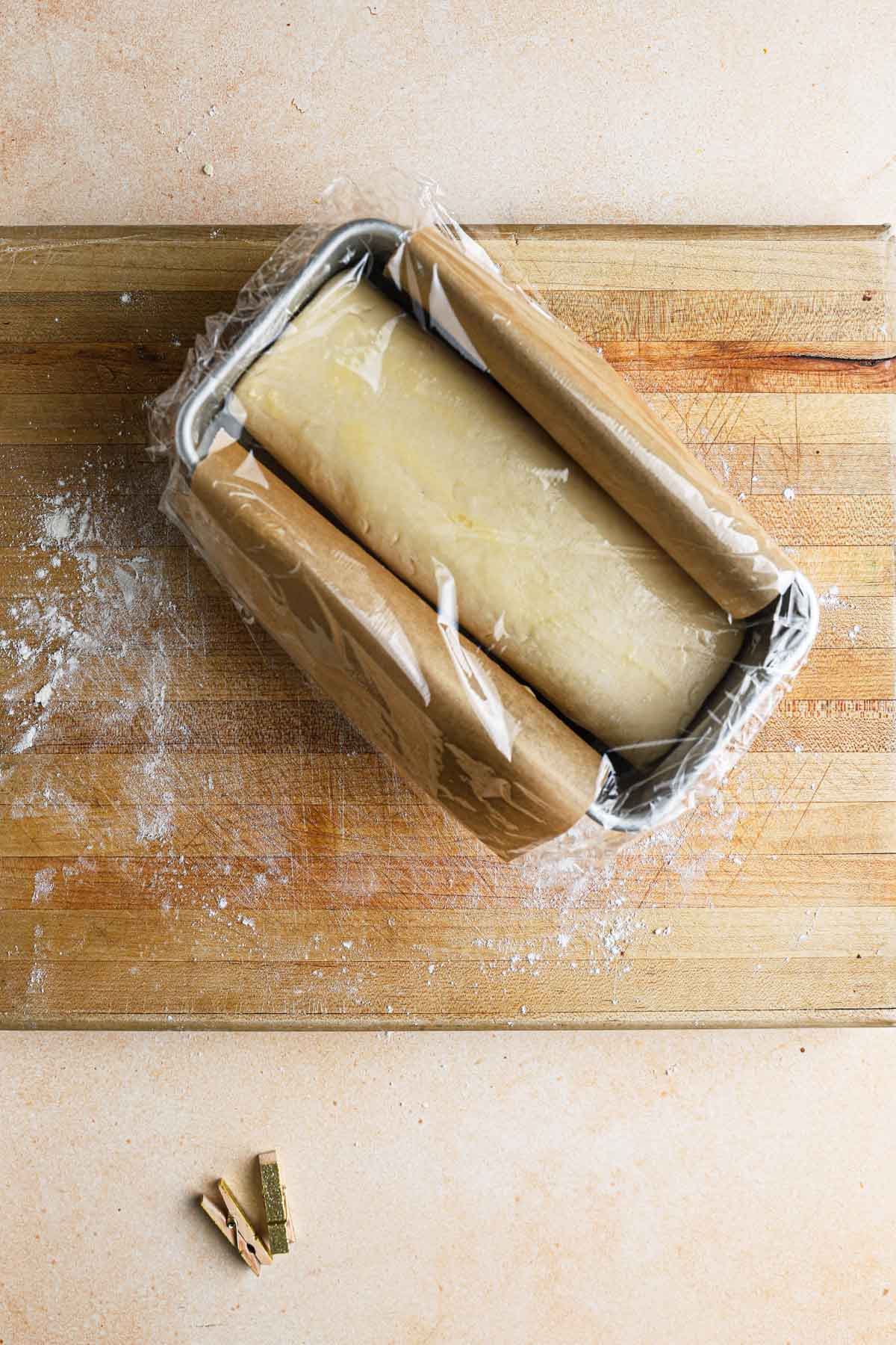 A pan with brioche dough topped with plastic wrap.