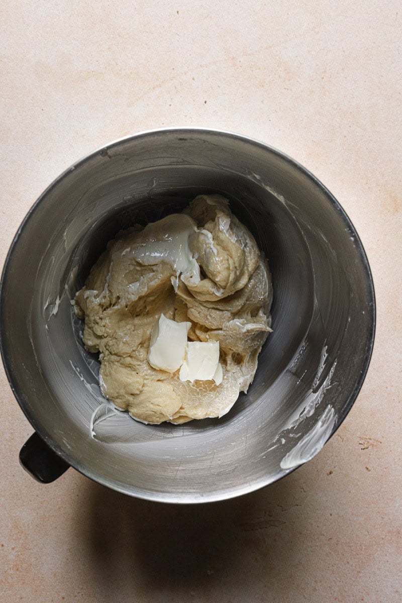 A mixer bowl with dough and butter pieces.