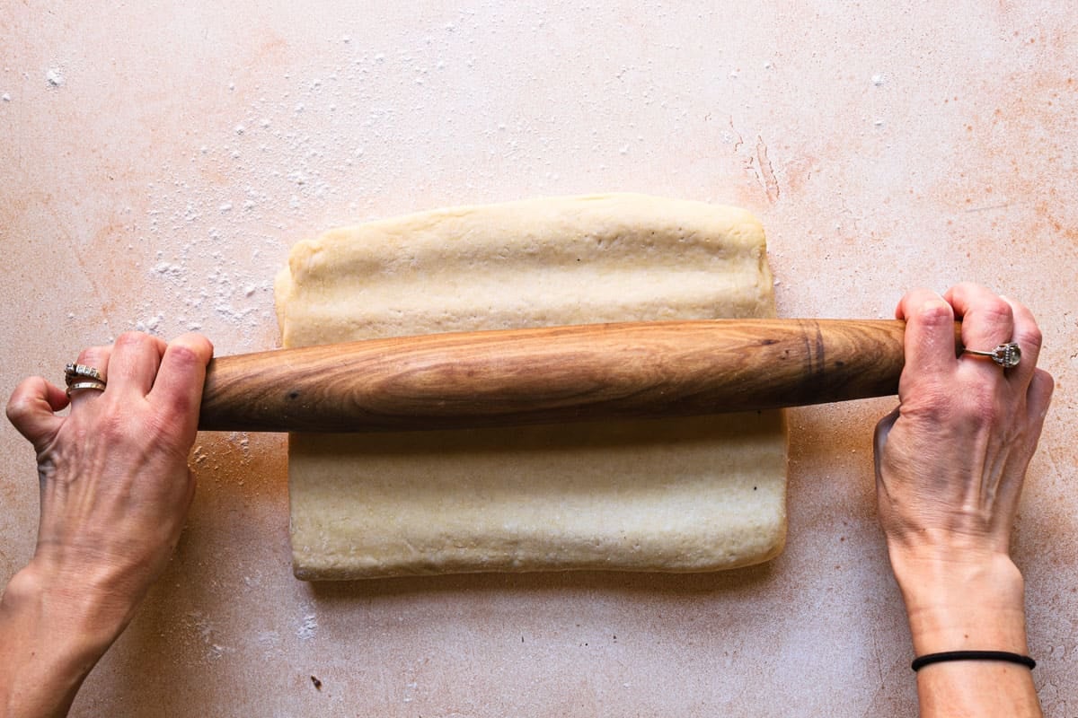 Hands tapping dough with a rolling pin