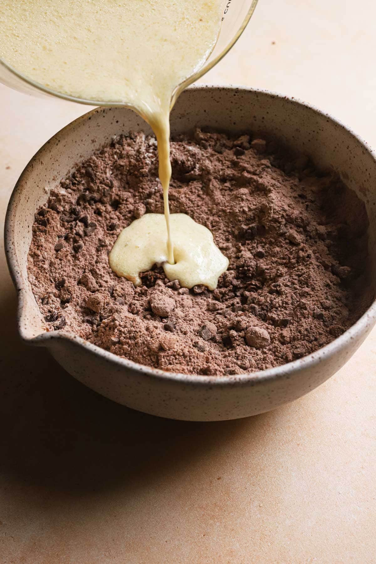 Pouring liquid mixture into a bowl with flour mixture.
